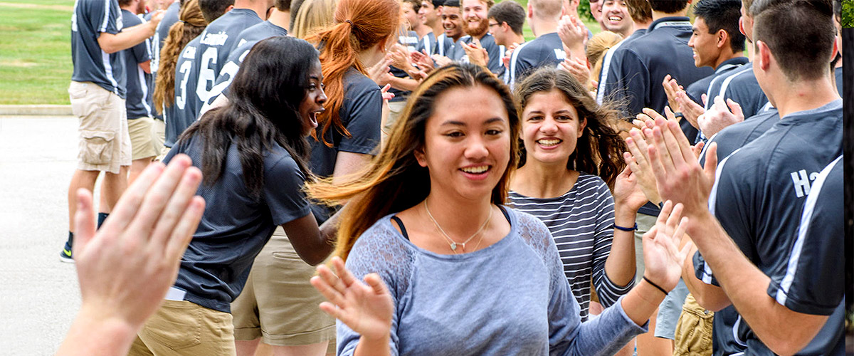 Image shows female freshmen smiling while running between two lines of resident assistants and other current 山Ƶ students receiving high fives. It’s part of the tradition of welcoming freshmen to campus.